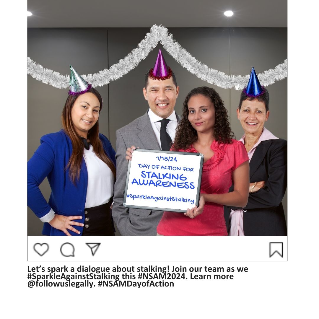 Four people standing in an office, wearing sparkly party hats and standing in front of a gray wall with white sparkly ribbon hanging. From left to right they are an Asian woman with long dark hair in a blue blazer and white shirt, a white man with short brown hair in a gray suit and white shirt, a Black woman with curly shoulder-length hair wearing a pink dress, and a white woman with short dark hair. wearing a black blazer and pink shirt.
